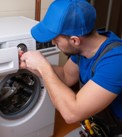 Worker repairing washing machine in laundry room.