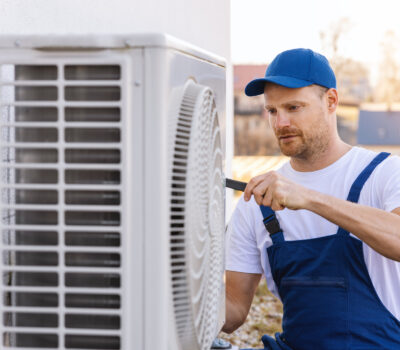 technician working on air conditioning or heat pump outdoor unit. HVAC service, maintenance and repair